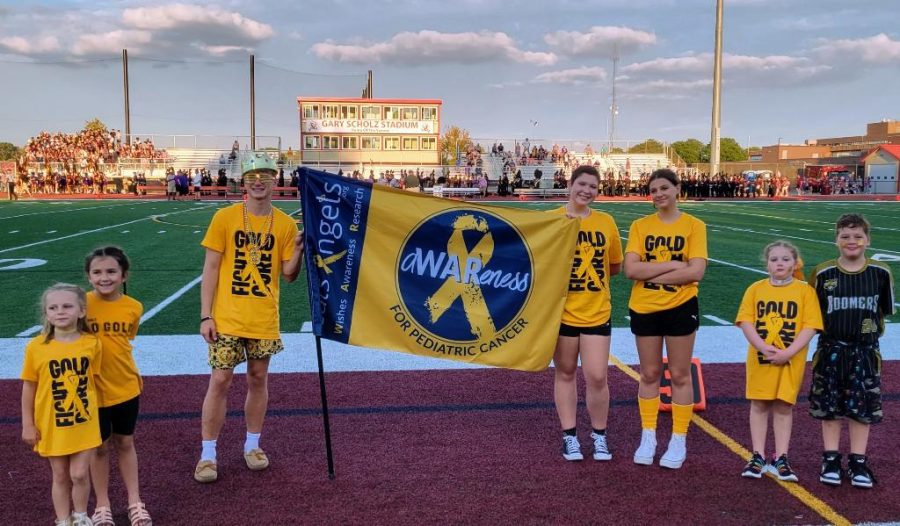 Cancer survivors from around Schaumburg, supportive siblings, and Saxon SuperFan hold a banner for Cal’s Angels during the Gold Out football game. 